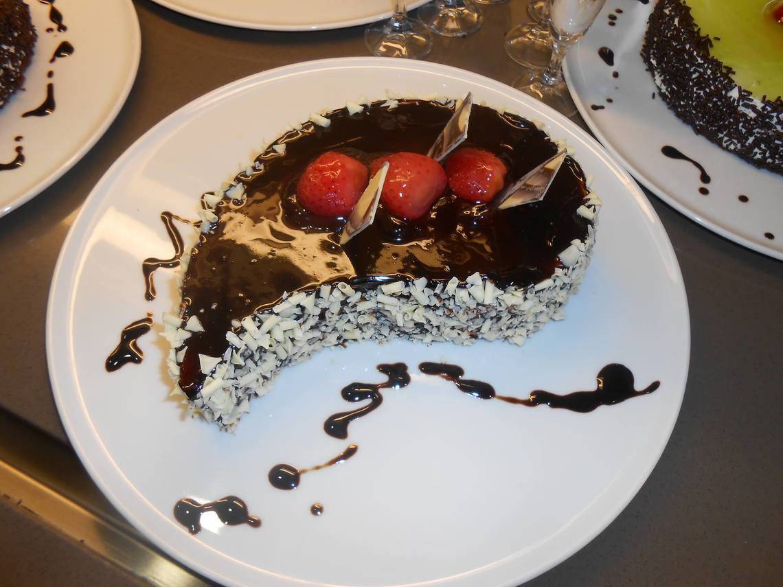 Ein Stück Schokoladenkuchen mit Erdbeeren auf einem weißen Teller mit Schokoladensauce.