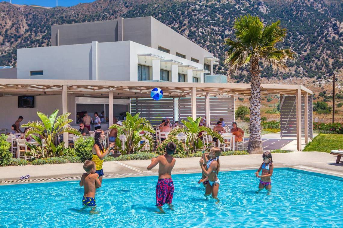 Kinder spielen im Pool vor dem Akti Palace Hotel mit einem Ball in der Luft.