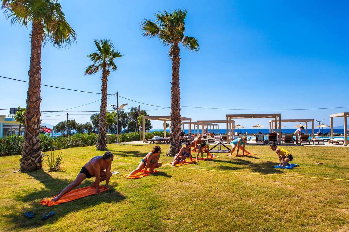 Yoga-Kurs auf der Wiese im Akti Palace Hotel mit Teilnehmern und Palmen im Hintergrund.