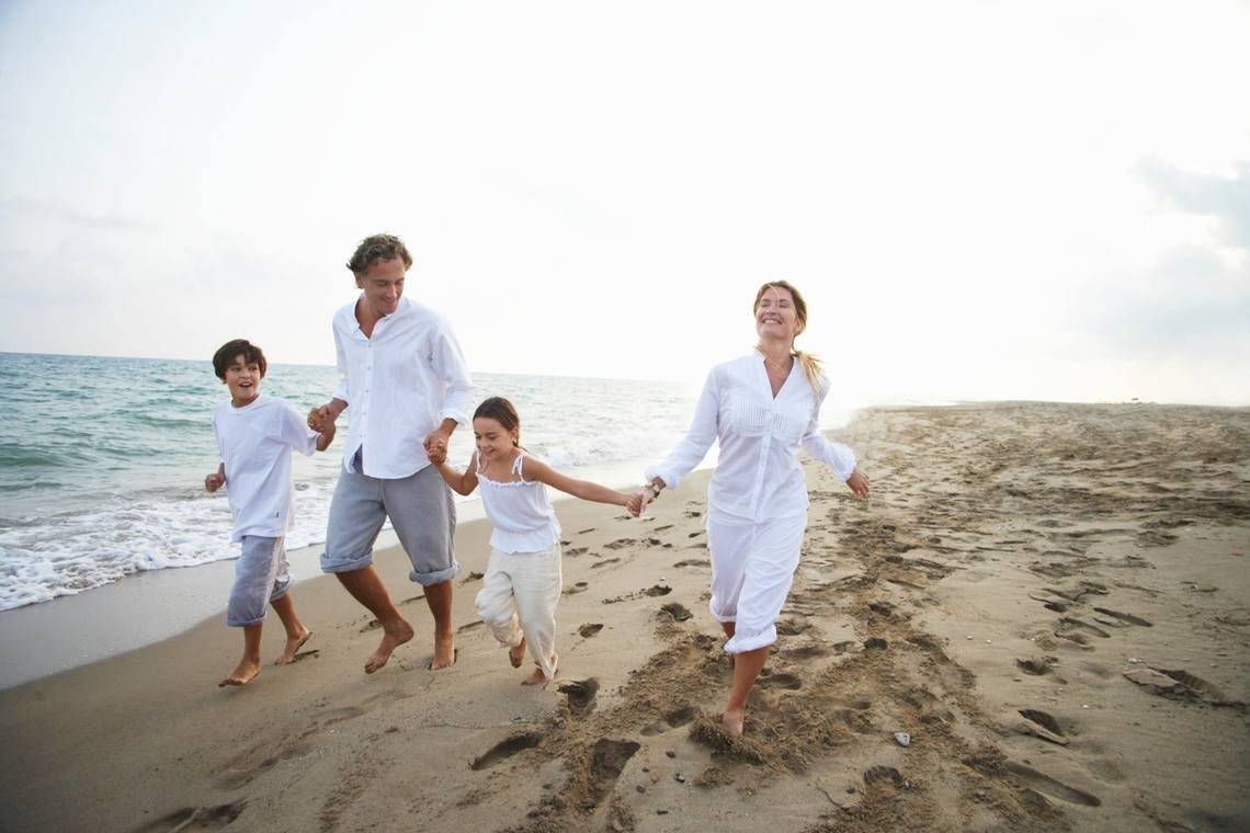 Eine Familie läuft am Strand, alle in weißen Kleidern, mit einem Lächeln auf den Gesichtern.
