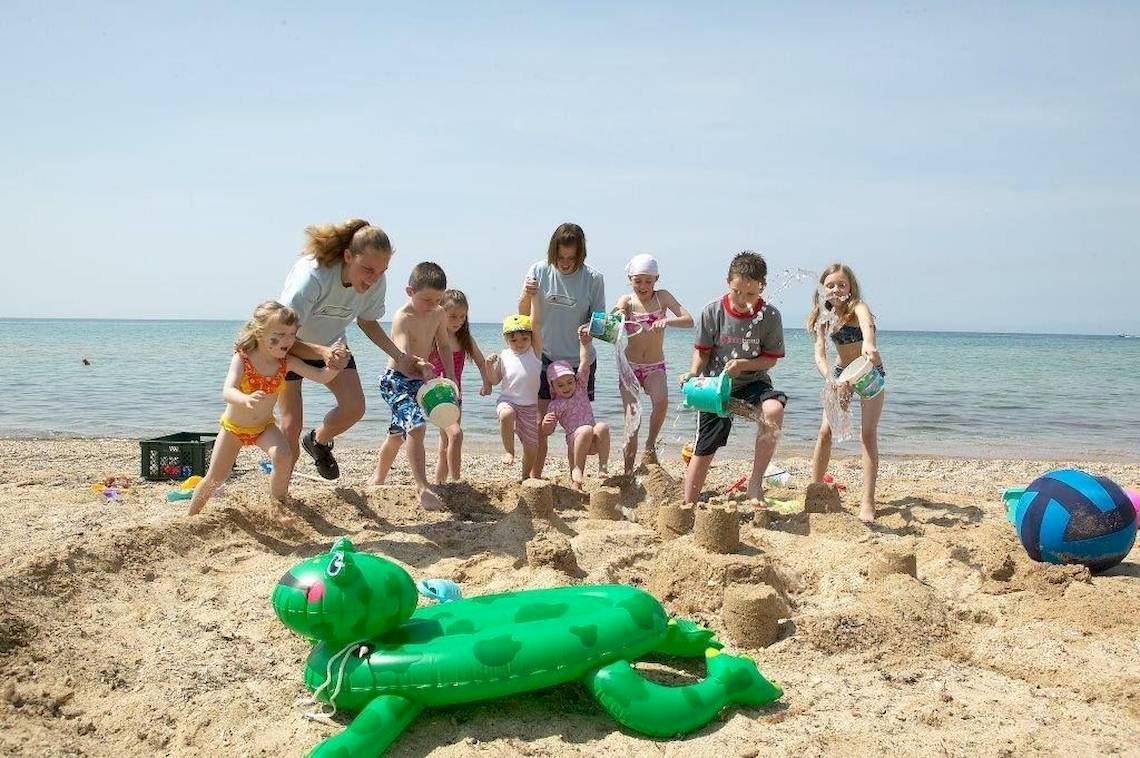 Familie und Kinder spielen am Strand des Ikos Oceania und bauen Sandburgen.