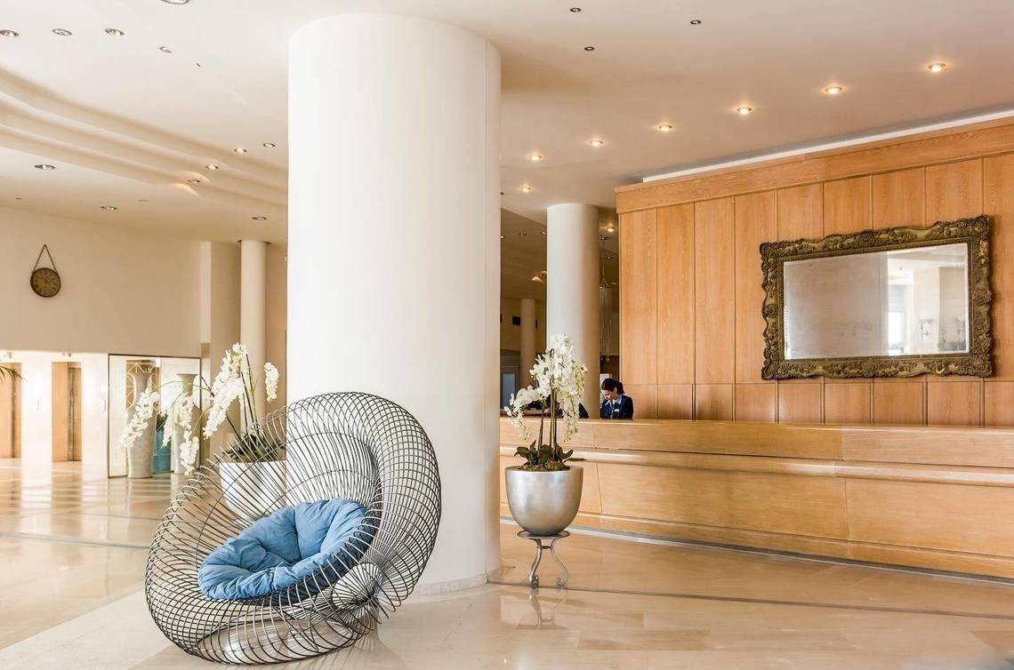 Lobby des Ikos Oceania Hotels mit Rezeption, Holzwänden und Sitzmöbeln.
