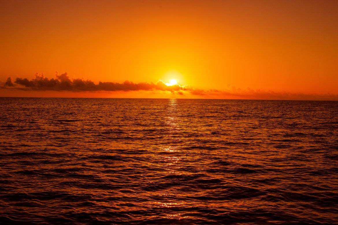 Sonnenuntergang über dem Meer mit reflektierenden Lichtern auf der Wasseroberfläche.