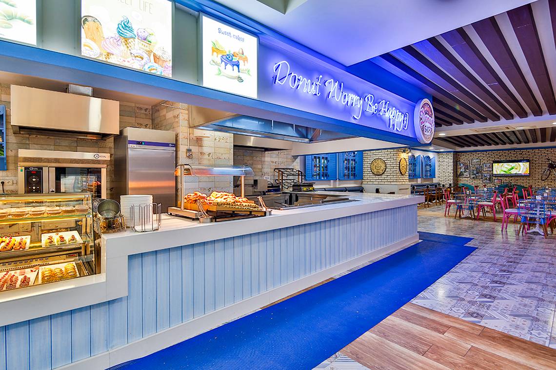 Innenansicht des Donut Wary Be Happy Restaurants im Crystal Admiral Resort Suites & Spa mit Theke, Backofen und Sitzbereich.