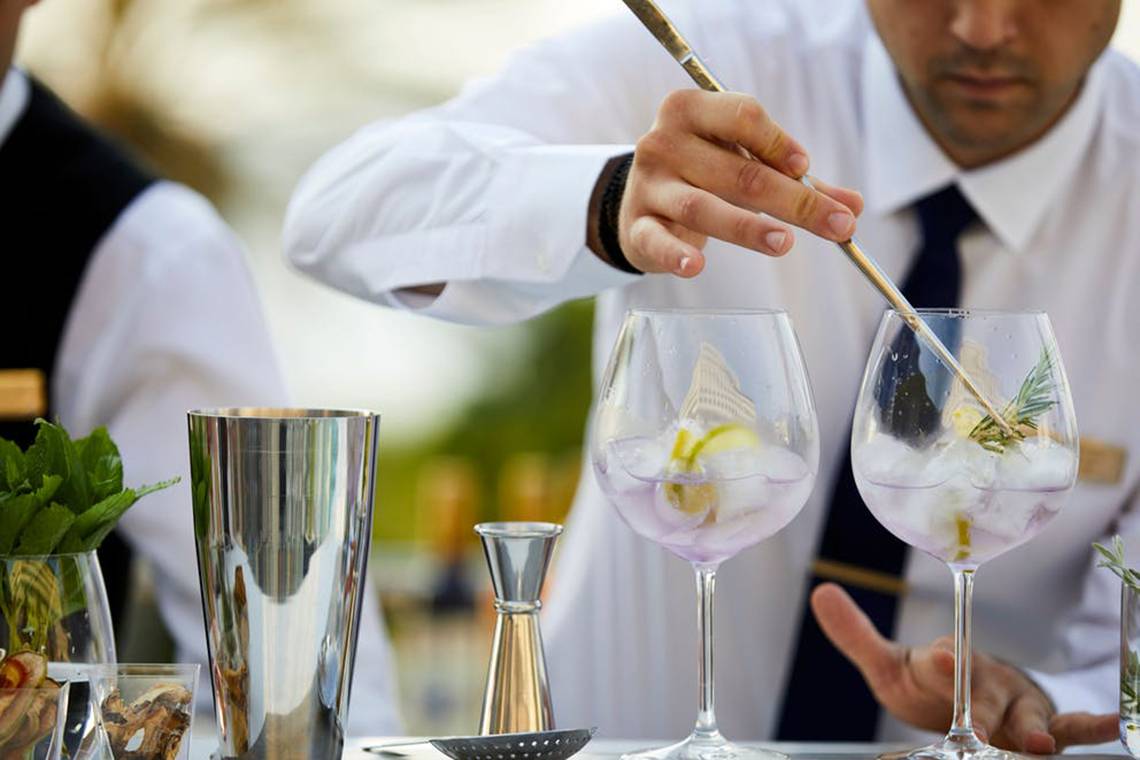 Ein Barkeeper bereitet Getränke in vollen Gläsern mit Eiswürfeln und Kräutern im Rhodes Bay Hotel & Spa zu.