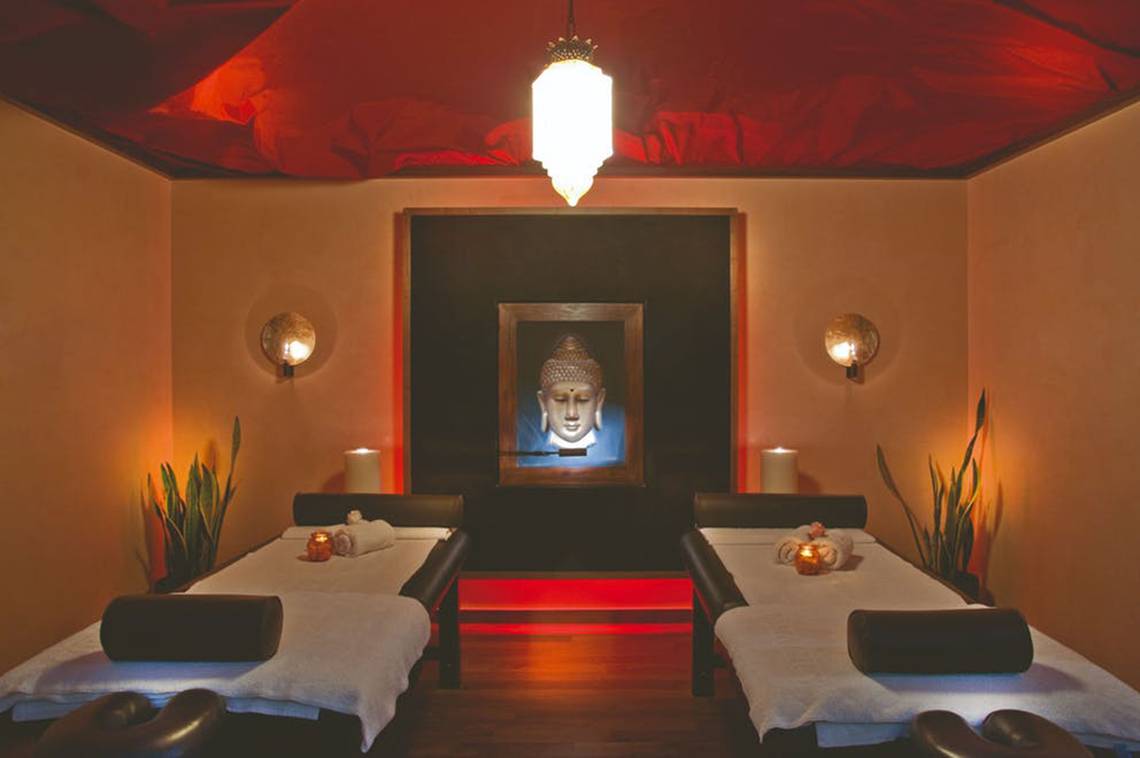 Massageraum im Rhodes Bay Hotel & Spa mit zwei Massagebetten, roten Akzenten und einem Buddha-Bild.