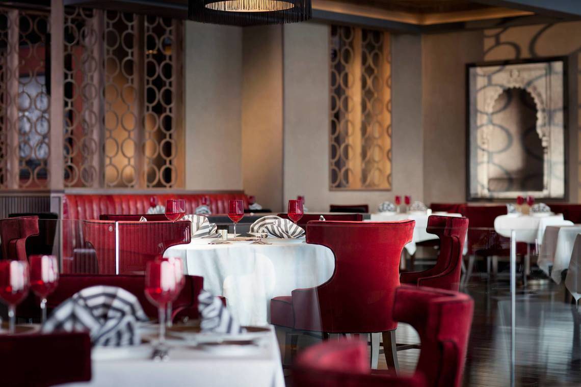 Innenansicht des Restaurants im Conrad Abu Dhabi Etihad Towers Hotel mit roten Stühlen und weißen Tischen.