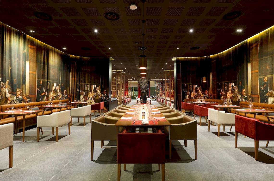 Innenansicht des Restaurants im TRS Coral Hotel mit langen Tischen, Stühlen und Gemälden an den Wänden.