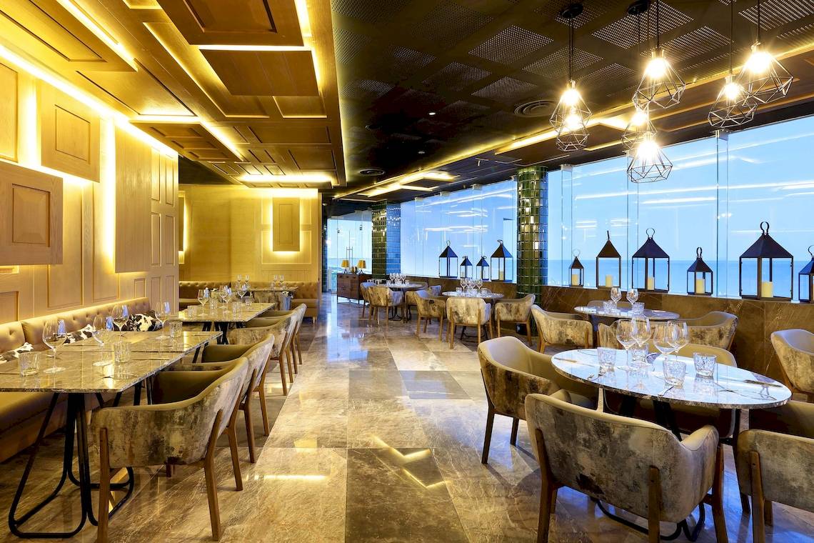 Innenansicht des Restaurants im TRS Coral Hotel mit runden Tischen, Stühlen und großen Fenstern.