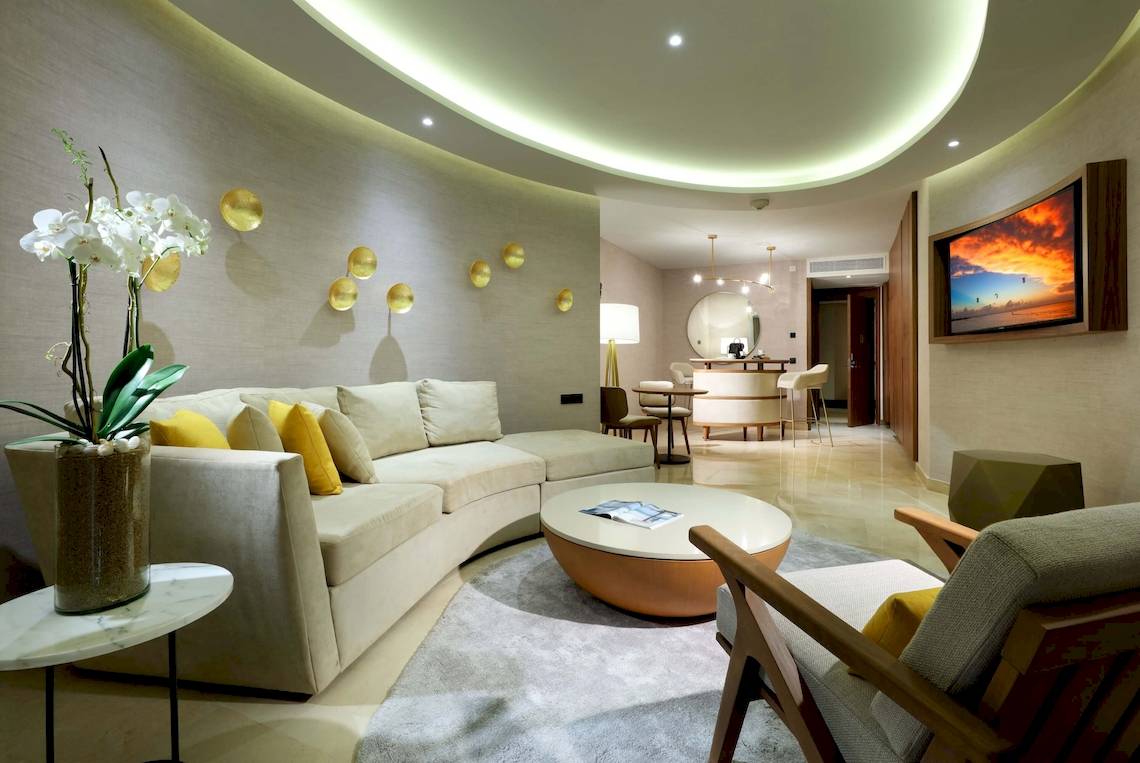 Innenansicht des Wohnzimmers im TRS Coral Hotel mit Rundsofa, Tisch und Fernseher.