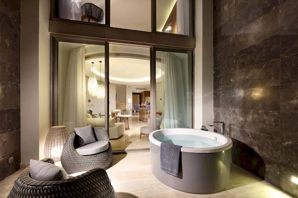 Das Badezimmer des TRS Coral Hotels mit einer Badewanne, Sesseln und Glastüren, die einen Blick auf den Innenhof bieten.