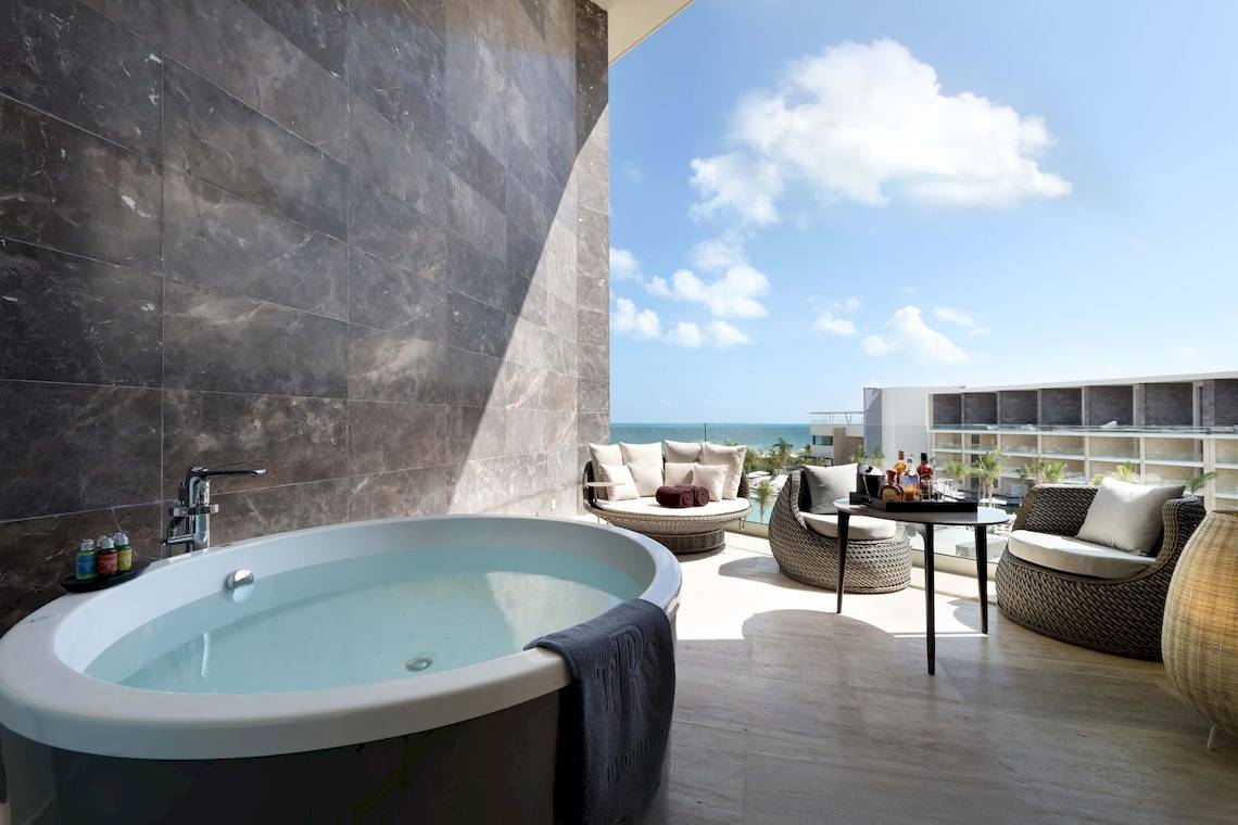 Balkon des TRS Coral Hotels mit Whirlpool und Meerblick, Möbeln und Flaschen auf einem Tisch.