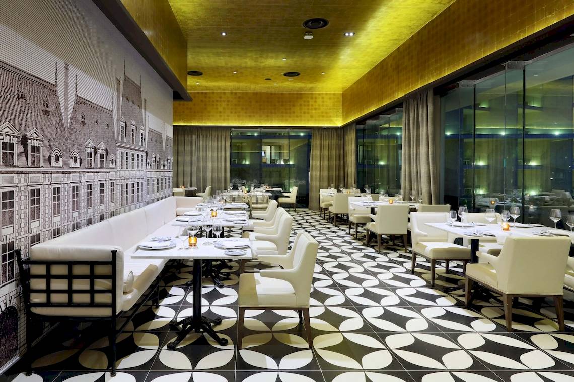 Restaurantbereich des TRS Coral Hotels mit gemustertem Boden, weißen Stühlen und Tischen, gelber Decke und Glaswänden.