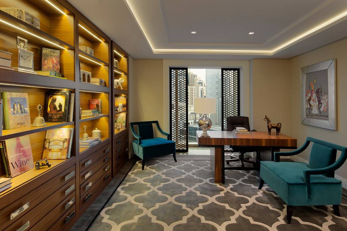 Innenansicht eines Zimmers im Taj Dubai Hotel mit Schreibtisch, Stühlen und Bücherregal.