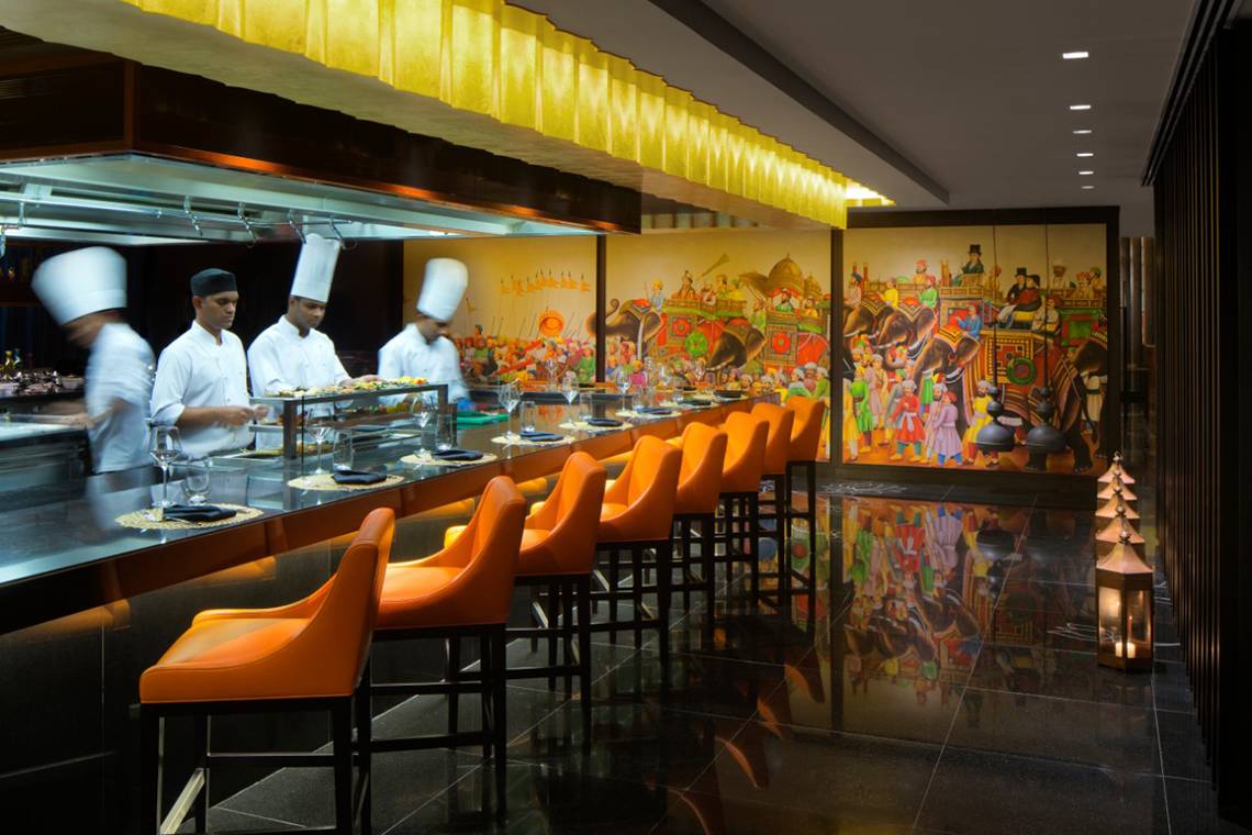 Innenbereich des Restaurants im Taj Dubai Hotel mit Küchenpersonal und kunstvollen Wandgemälden.