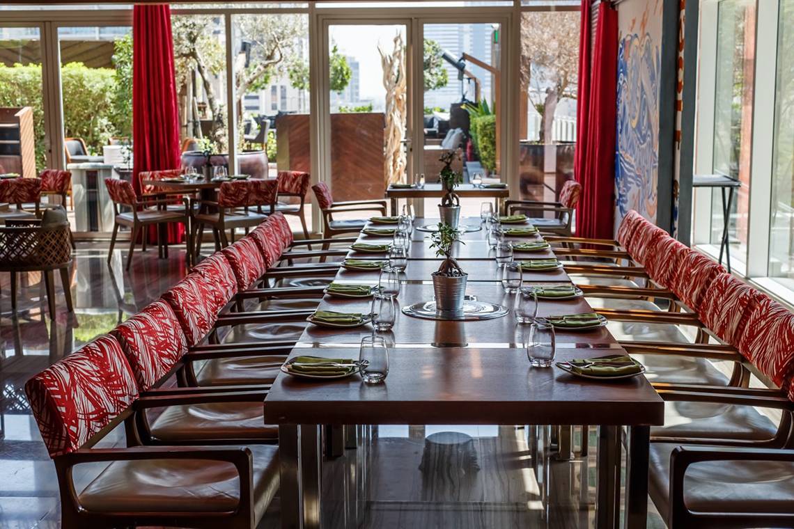 Innenbereich des Restaurants im Taj Dubai mit langen Holztischen und roten Sesseln.