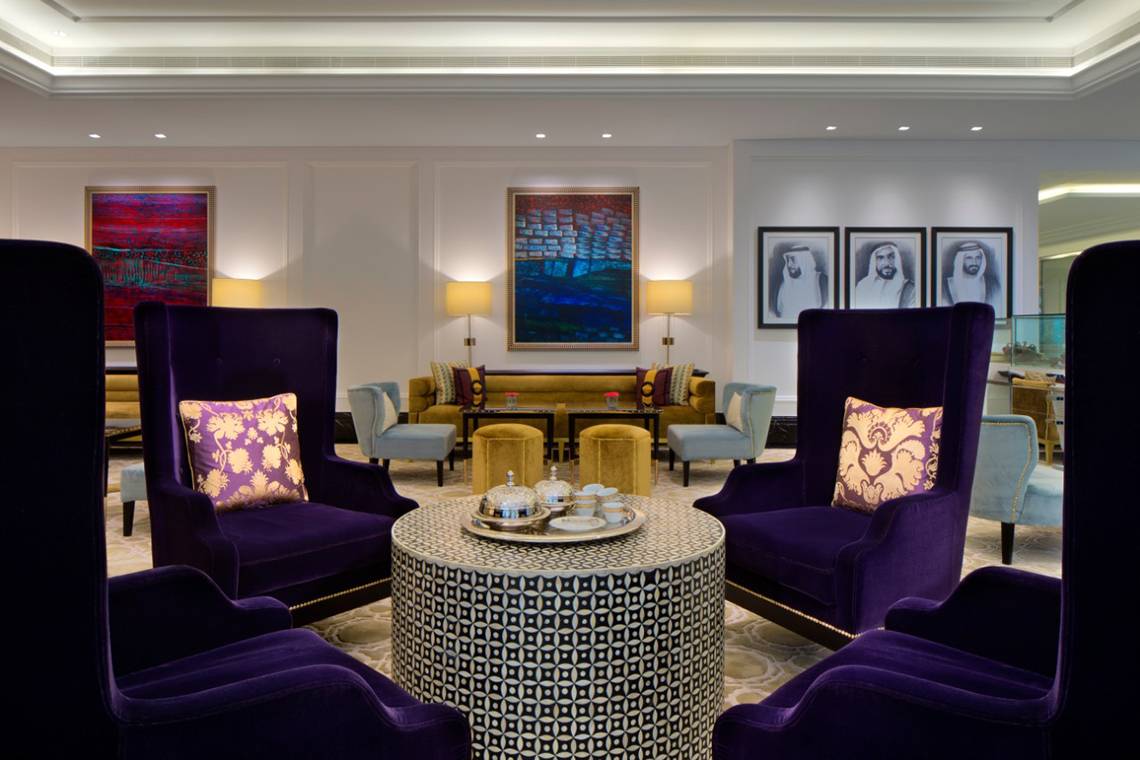 Loungebereich im Taj Dubai Hotel mit violetten Sesseln, runden Tisch und Kunstwerken an der Wand.
