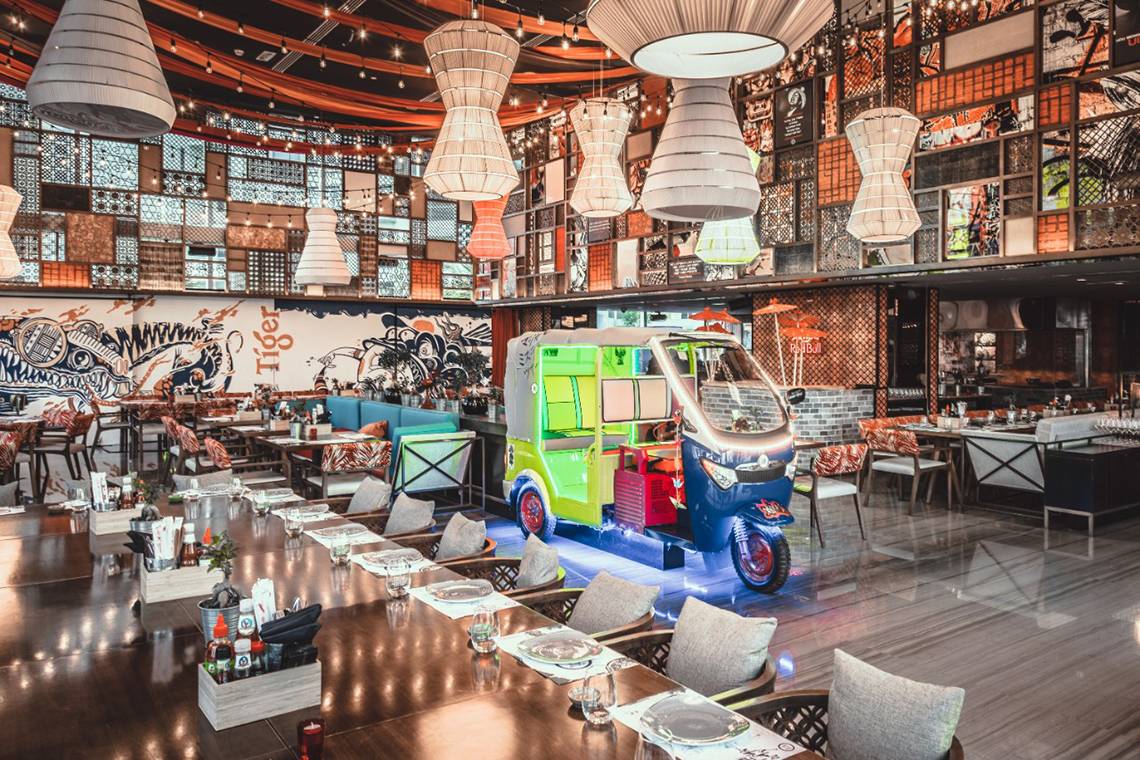 Innenansicht eines Restaurants mit Tuk-Tuk-Dekor und farbigen Wandmalereien.