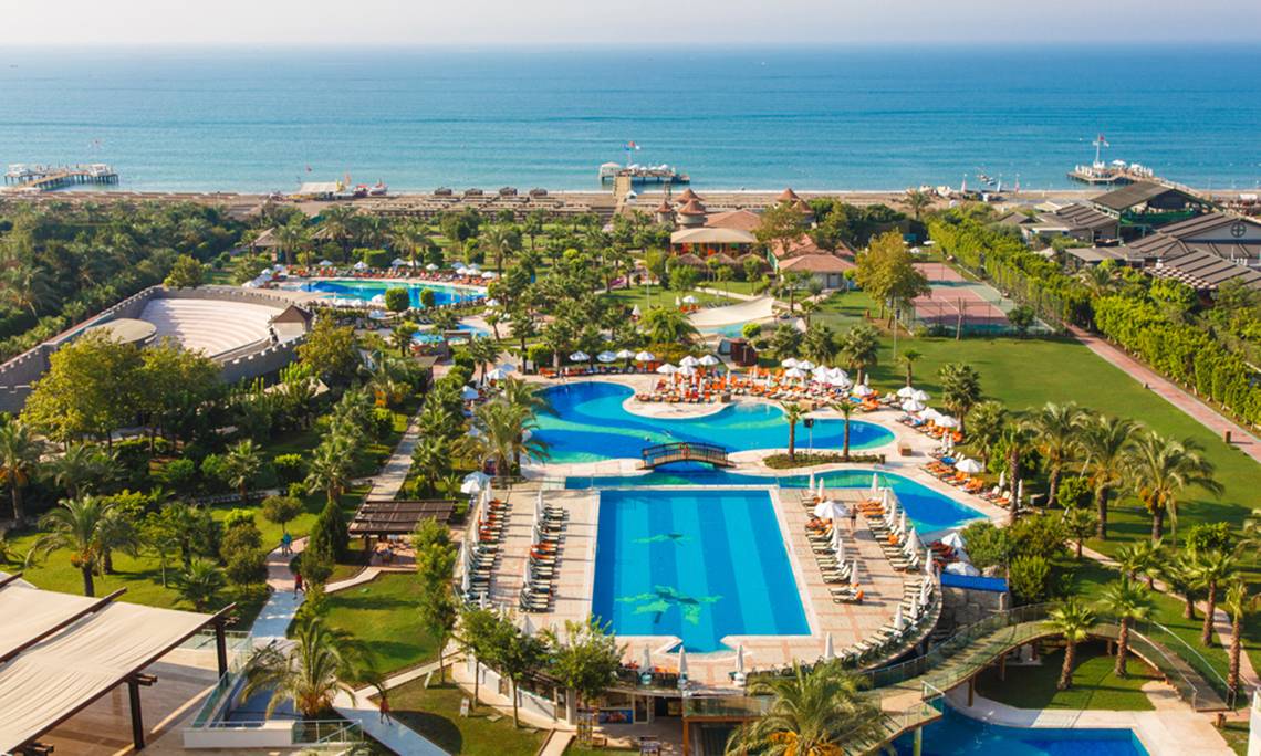 Luftaufnahme des Sherwood Exclusive Lara Resorts mit Swimmingpools, Sonnenliegen und Blick auf das Meer.
