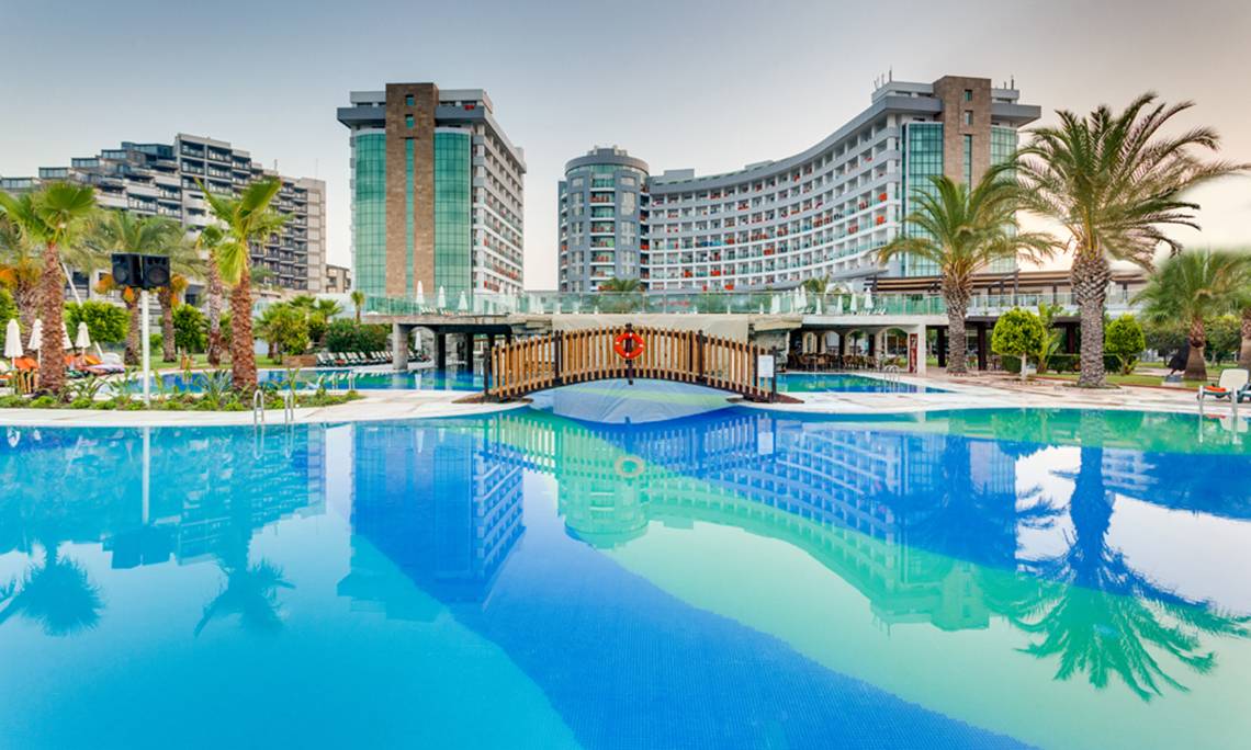 Ein Swimmingpool vor dem Sherwood Exclusive Lara Hotel mit einem Holzsteg und Palmen.