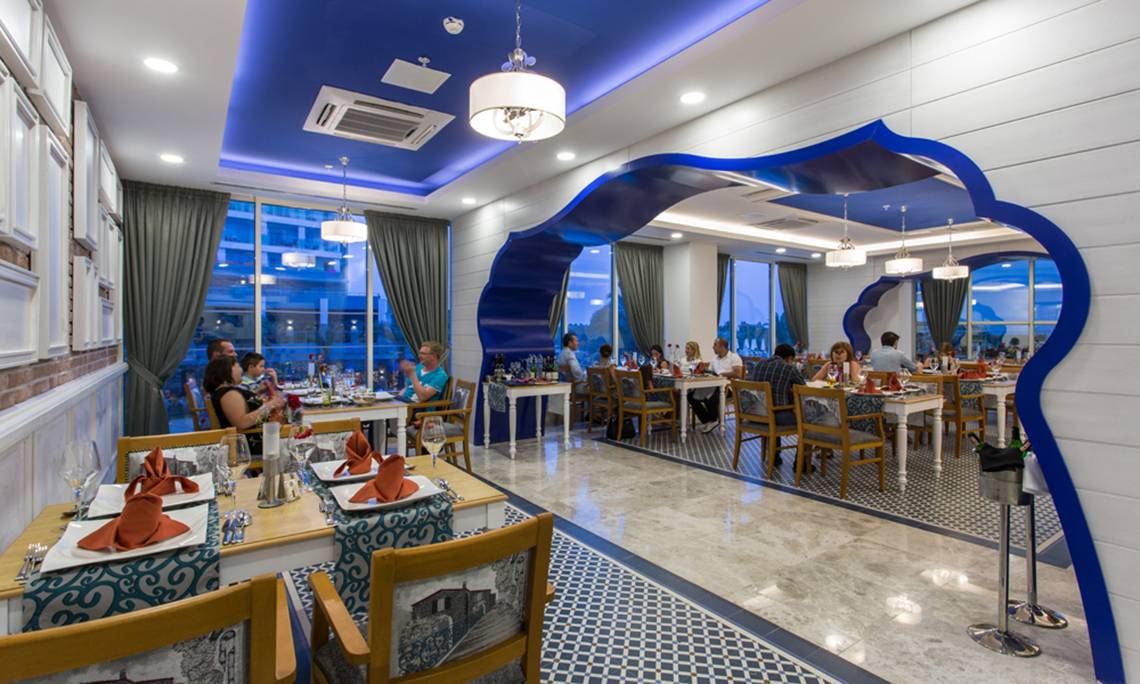 Restaurant im Sherwood Exclusive Lara Hotel mit blauen Akzenten und Gästen, die an Tischen sitzen.