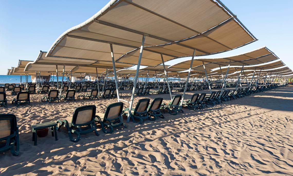 Reihen von Sonnenliegen unter Sonnenschirmen am Strand des Sherwood Exclusive Lara Hotels.