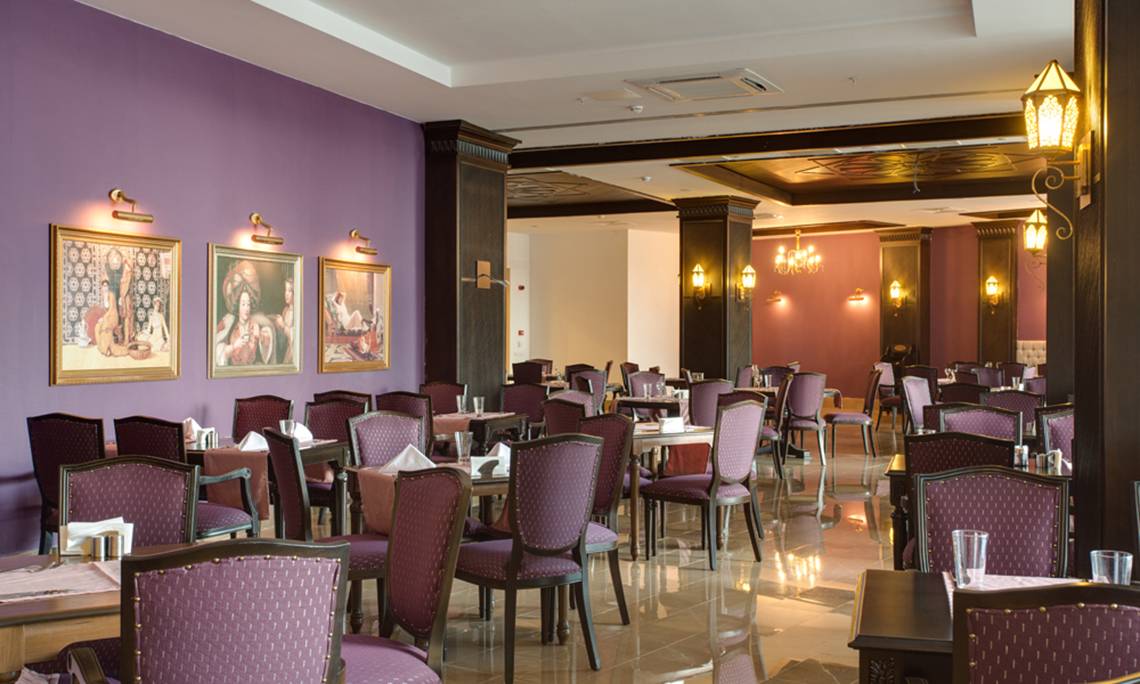 Sherwood Exclusive Lara Hotel Restaurant mit lila Wänden, gepolsterten Stühlen und gedeckten Tischen.