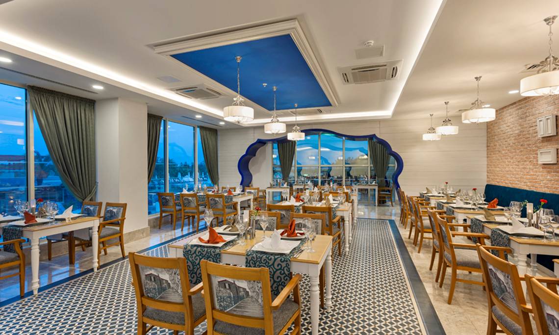 Innenansicht des Restaurants des Sherwood Exclusive Lara Hotels mit blauer Decke und großen Fenstern.