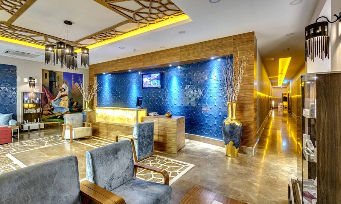 Lobby des Sherwood Exclusive Lara Hotels mit blauen Wänden, goldenem Vasen, Sitzbereich und Fernseher.