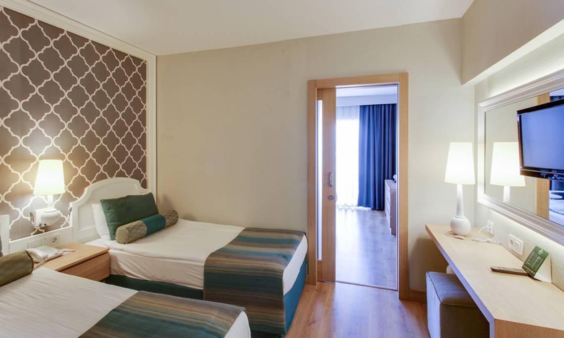 Innenansicht eines Doppelzimmers im Sherwood Exclusive Lara Hotel mit zwei Betten, Dekor, Lampen und Fernseher.