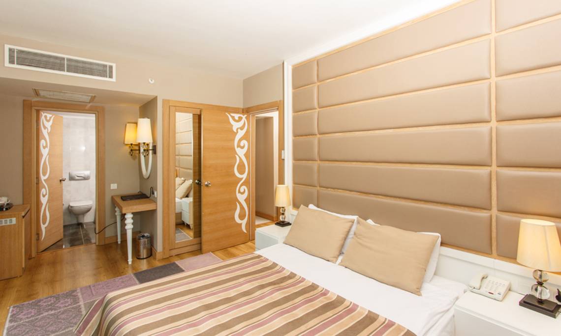 Hotelzimmer im Sherwood Exclusive Lara mit Doppelbett, Kissen, Nachttischen und cremefarbenen Wänden.