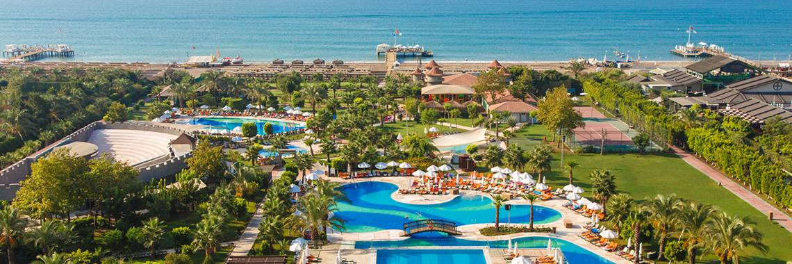 Luftaufnahme des Sherwood Exclusive Lara Resorts mit Swimmingpools, Sonnenliegen und Hotels am Meer.