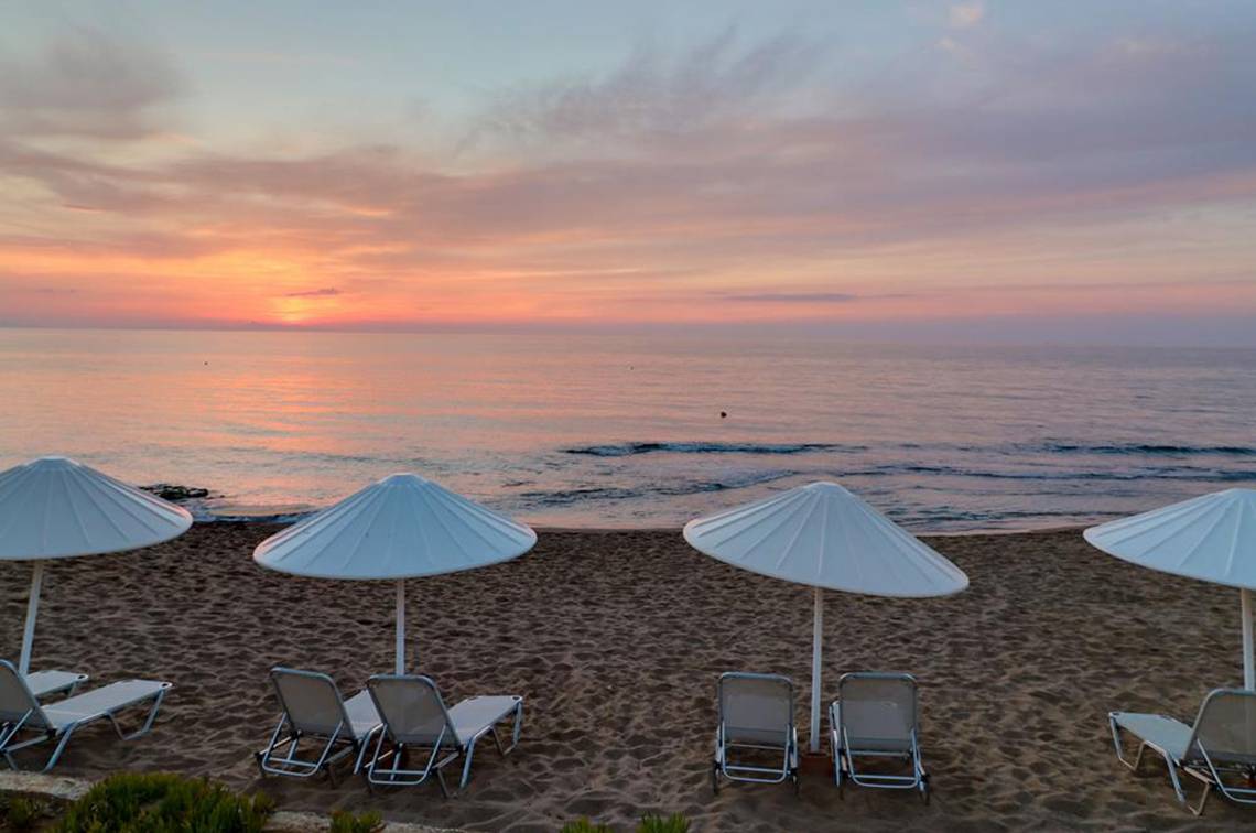Sonnenuntergang am Strand des Creta Star Hotels mit weißen Sonnenschirmen und Liegestühlen.