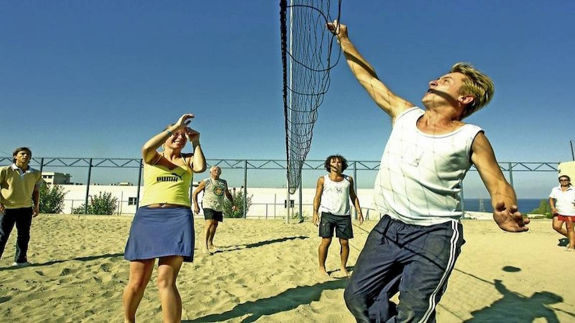 Eine Gruppe von Menschen spielt Volleyball auf einem Sandplatz unter einem blauen Himmel.