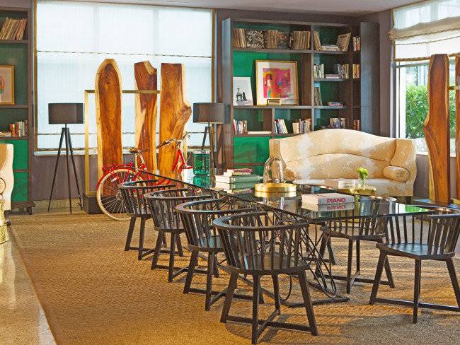 Lobby-Bereich des Kimpton Surfcomber Hotels mit Glastisch, Stühlen und Bücherregal.