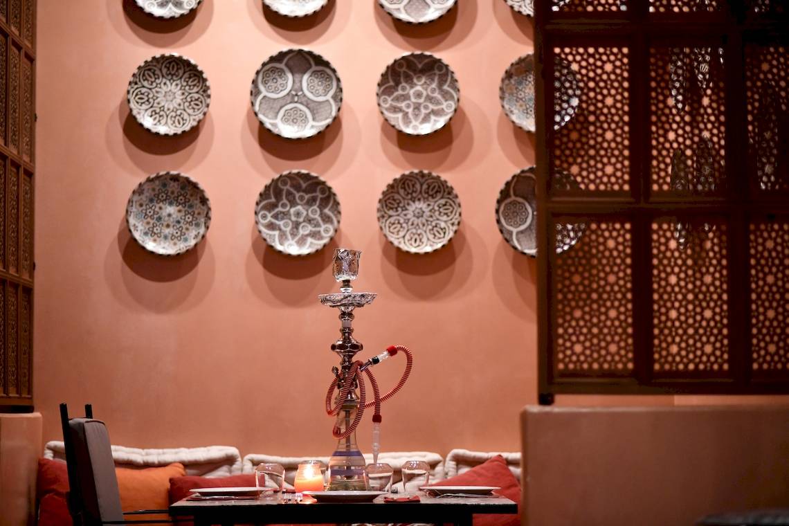 Tisch im Westin Resort Costa Navarino mit einer Narghile und dekorativen Tellern an der Wand.