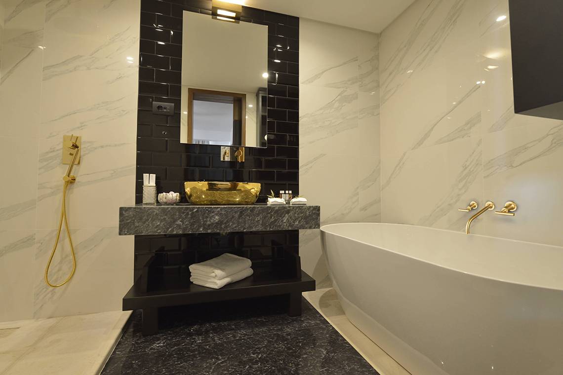 Luxuriöses Badezimmer im Domes of Elounda, Autograph Collection mit Marmorfliesen und goldenen Armaturen.