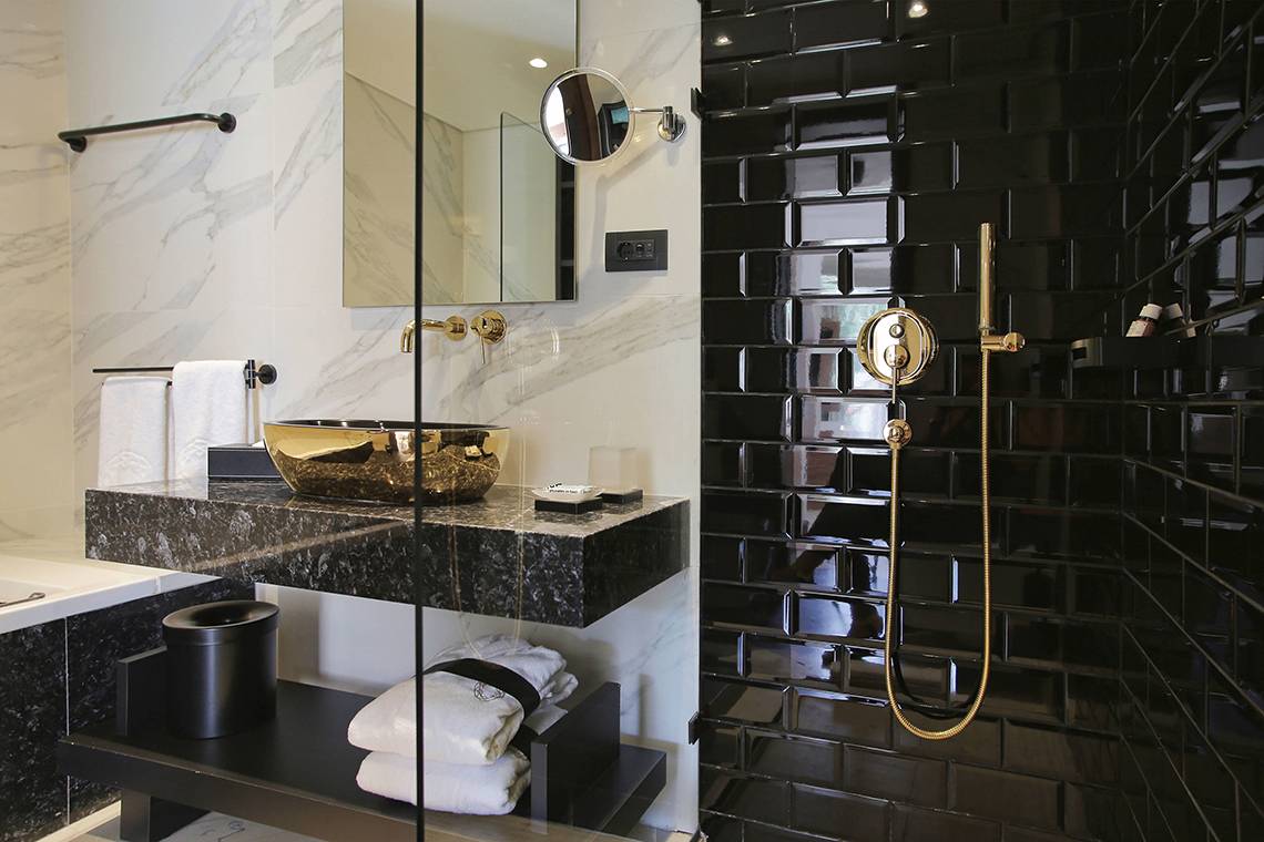 Ein Badezimmer mit schwarzen Fliesen und goldenen Armaturen, inklusive eines schwarzen Waschbeckens und einer goldenen Duschbrause.