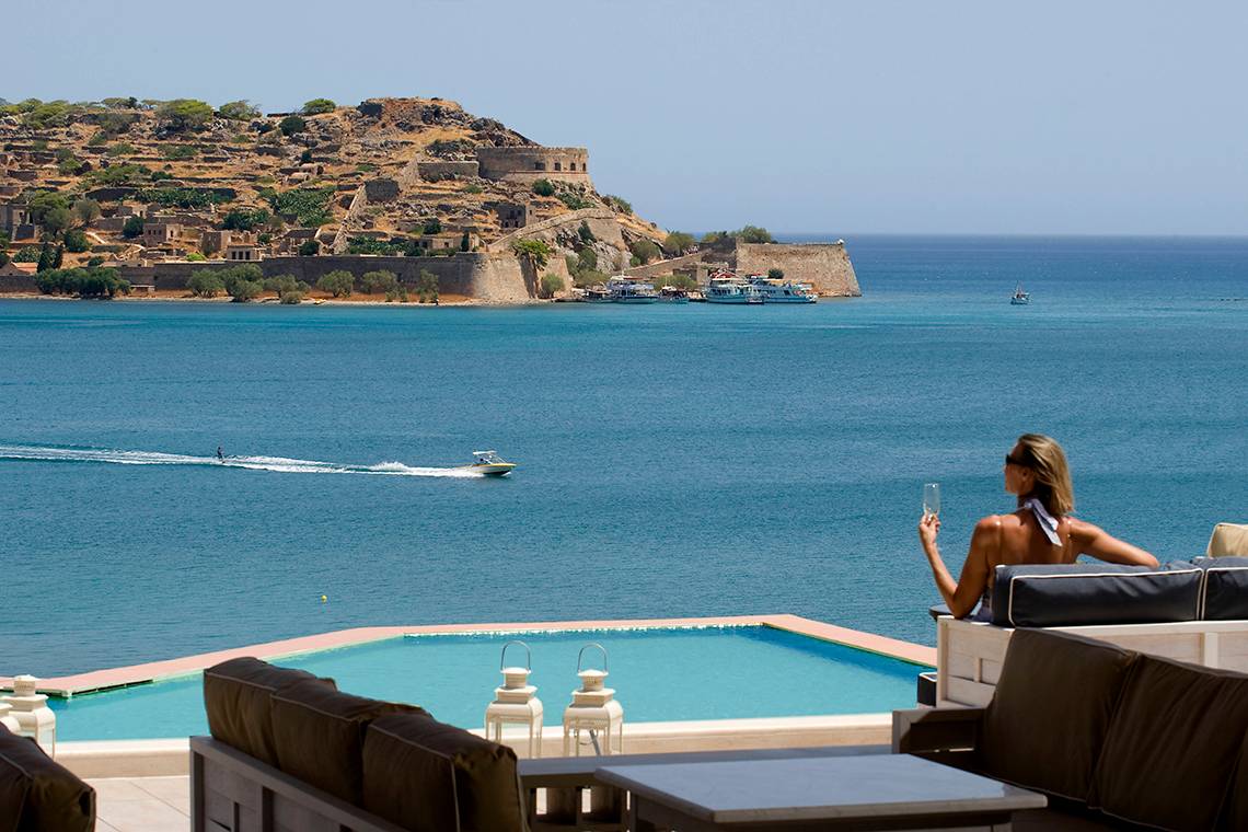 Aussicht auf das Meer vom Domes of Elounda, Autograph Collection Hotel mit einer Frau, die einen Cocktail hält.