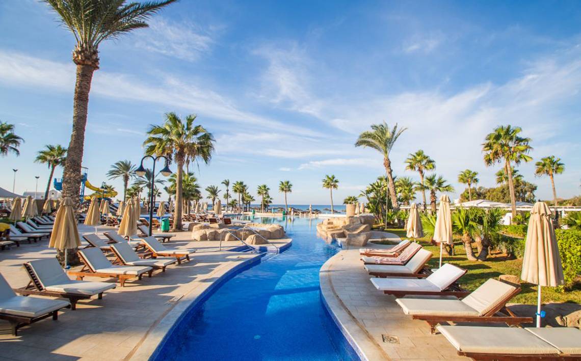 Pool-Loungebereich im Adams Beach Hotel mit Sonnenliegen und Palmen