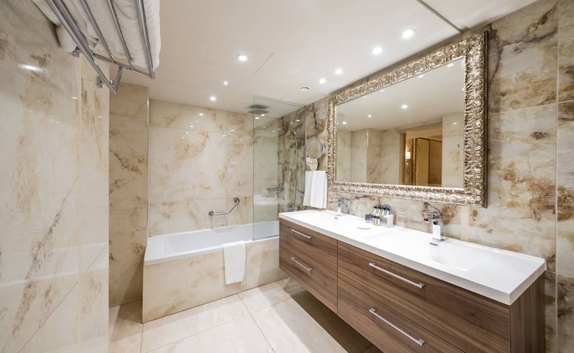 Ein elegantes Badezimmer im Adams Beach Hotel mit Marmorwänden, Badewanne und Doppelwaschbecken.