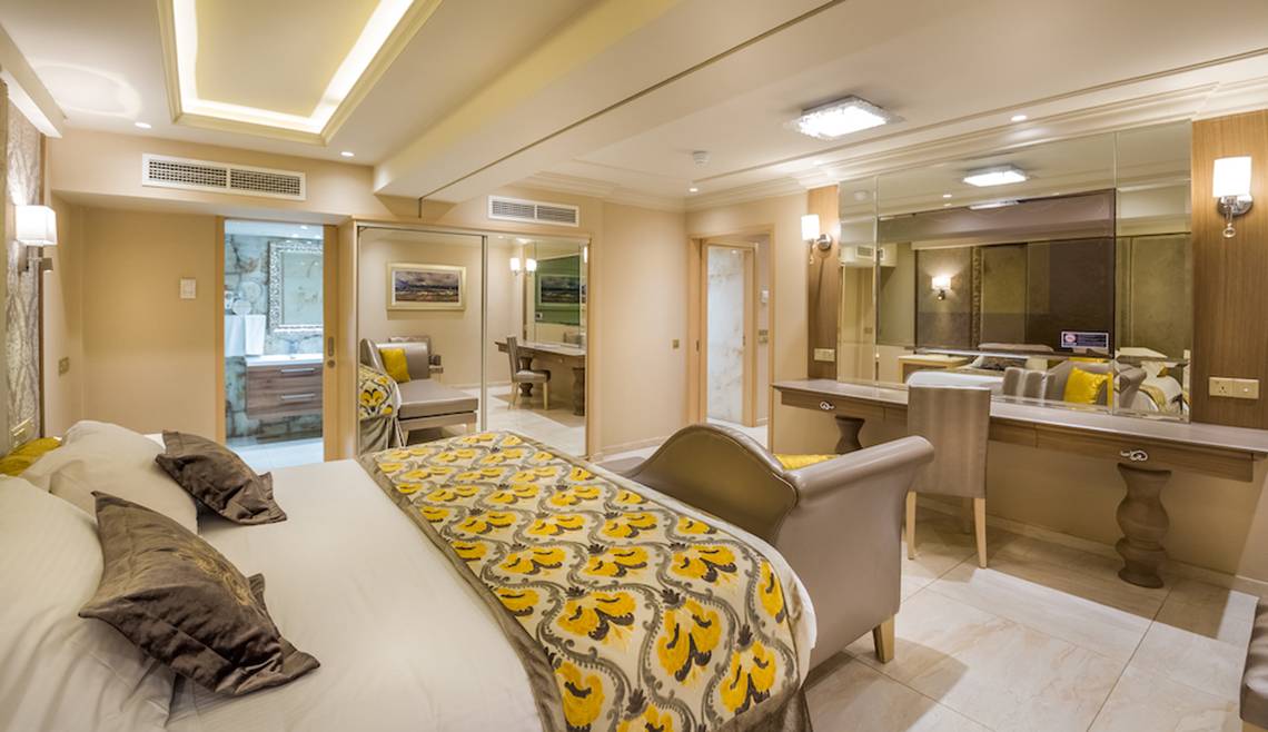Innenansicht eines Schlafzimmers im Adams Beach Hotel mit Bett, Schreibtisch und Spiegeln.