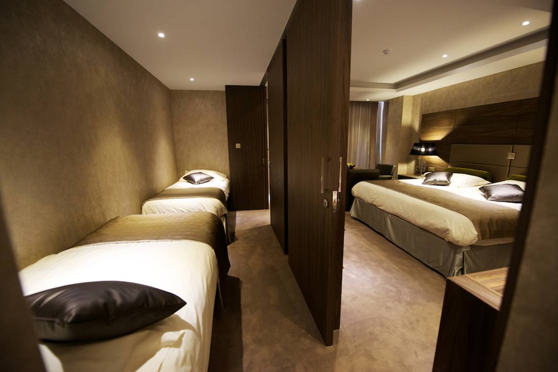 Schlafzimmer im Adams Beach Hotel mit mehreren Betten und dunklen Holzmöbeln.