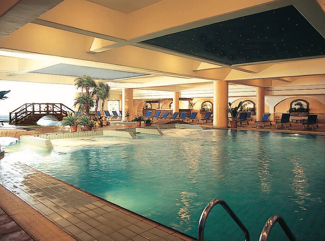 Ein großer Pool im Adams Beach Hotel mit einer Brücke und Liegestühlen