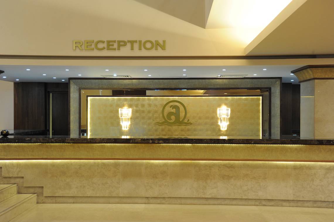 Rezeptionsbereich des Adams Beach Hotels mit goldenem Schild und illuminierten Logos.