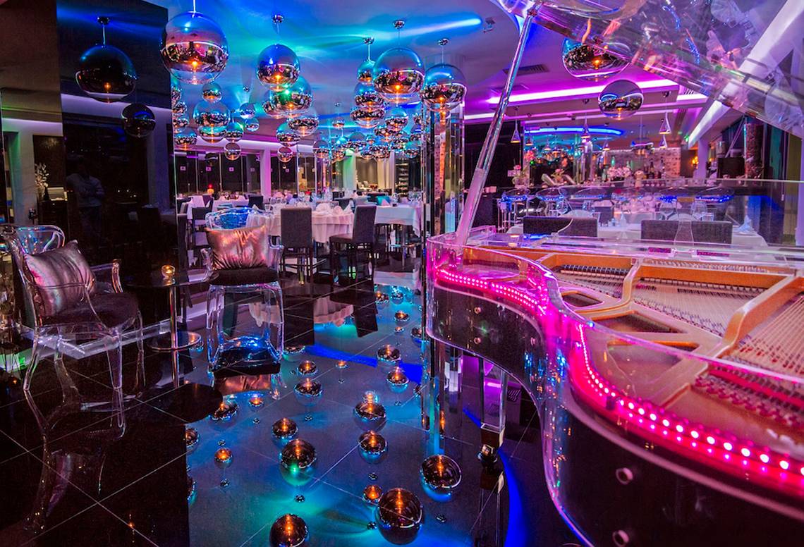 Innenraum des Adams Beach Hotel mit spiegelnden Böden, runden Lichtern und einer großen Glasklavier.