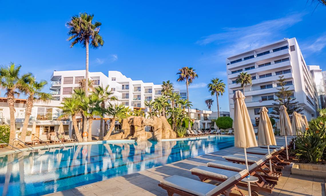 Außenbereich des Adams Beach Hotels mit Pool, Liegestühlen und Palmen