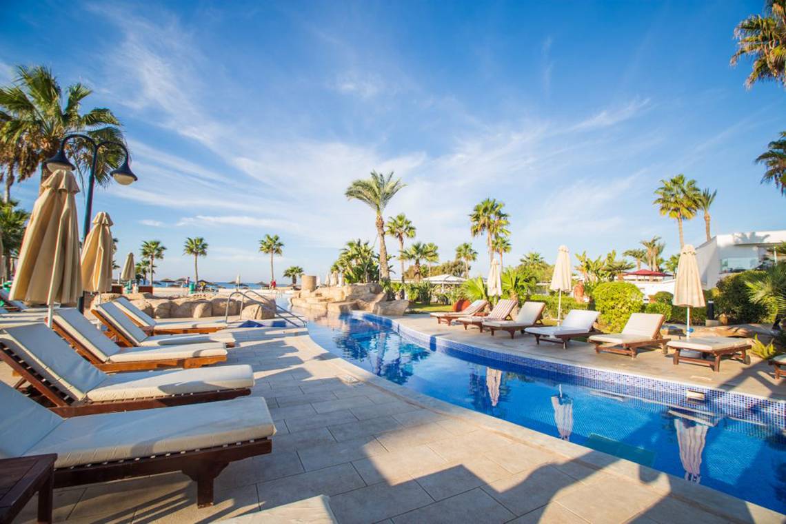 Außenpoolbereich des Adams Beach Hotels mit Liegestühlen und Palmen