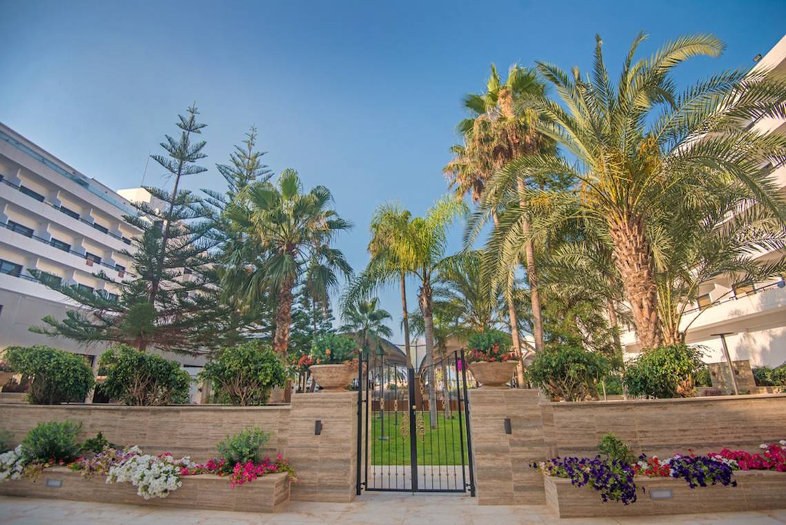 Eingang des Adams Beach Hotels mit geschwungenen Toren und üppiger Gartenanlage.