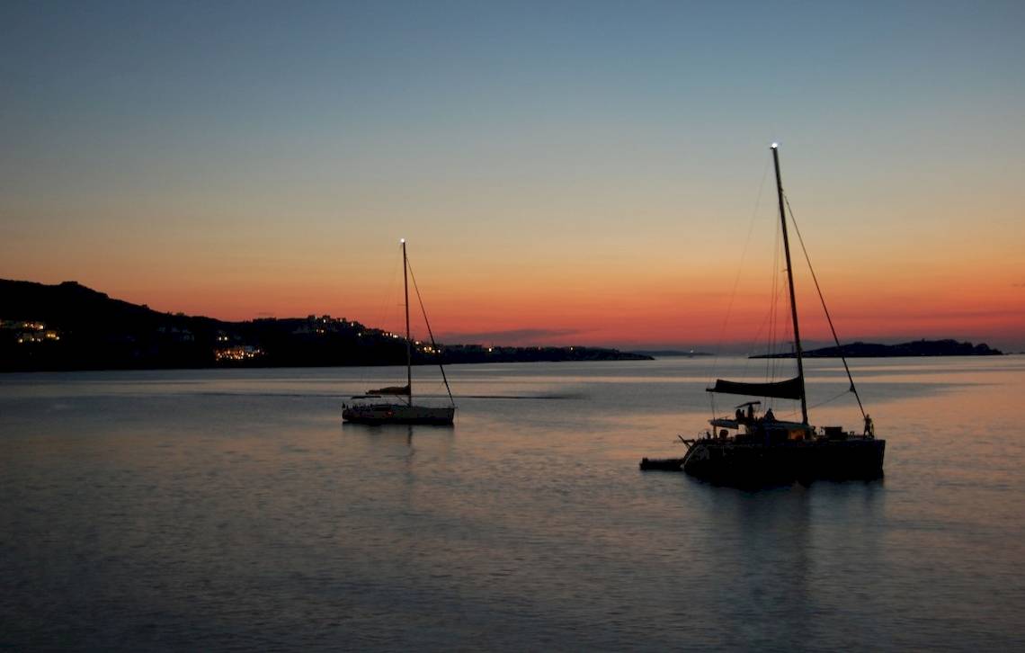 Zwei Segelboote im Wasser bei Sonnenuntergang mit leuchtenden Mastspitzen.